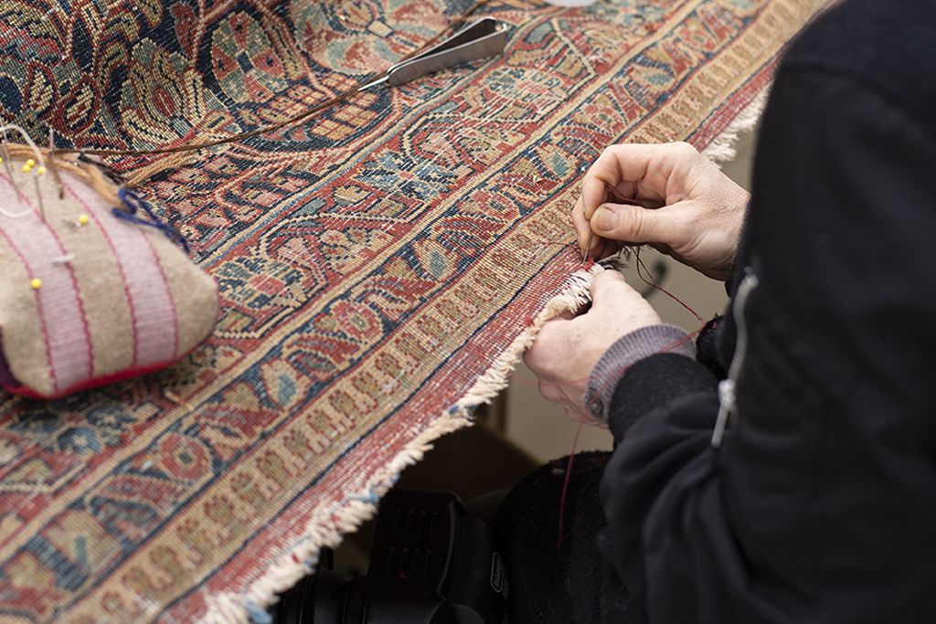 An oriental rug with damage being repaired by hand